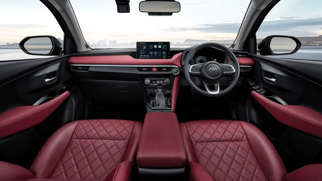 Toyota Yaris interior com couro vermelho, a foto também mostra a tela multimídia volante e o retrovisor.