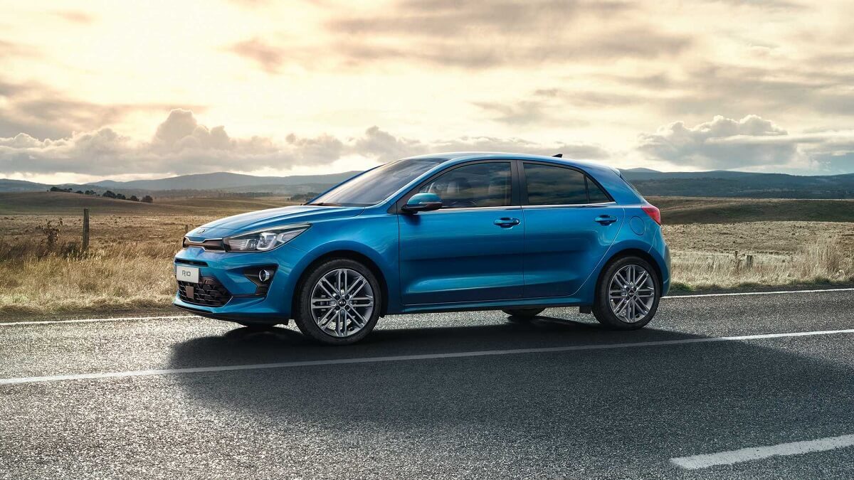 Foto lateral de um Kia Rio em 2023 azul andando em uma estrada