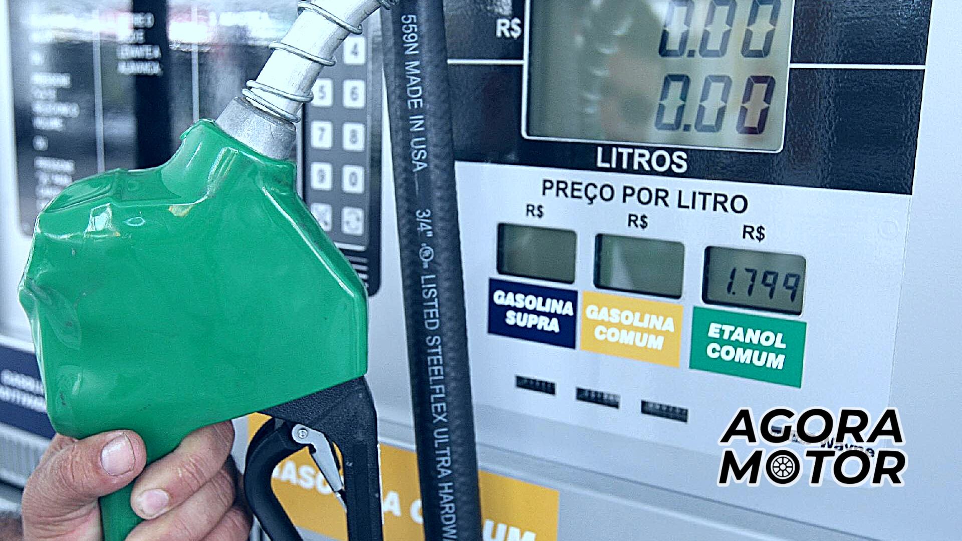 Foto de uma pessoa segurando um bico de bomba de gasolina, ao fundo preço e litros