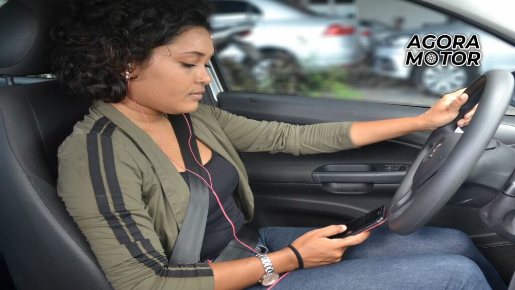 Foto de uma mulher com fone de ouvido, mexendo no celular e dirigindo
