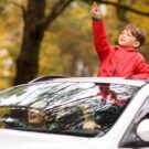Criança para fora do carro em teto solar com família no carro.