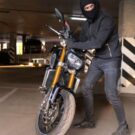 Homem roubando moto parada em estacionamento.