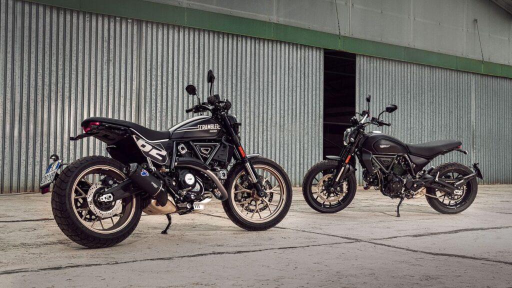 Duas Ducati Scrambler Icon 2025 em frente de galpão.