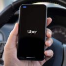 um homem dentro do carro segurando o celular com a logo do uber na tela.