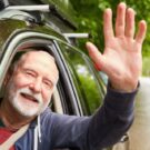 Um idoso levantando a mão dentro do carro.