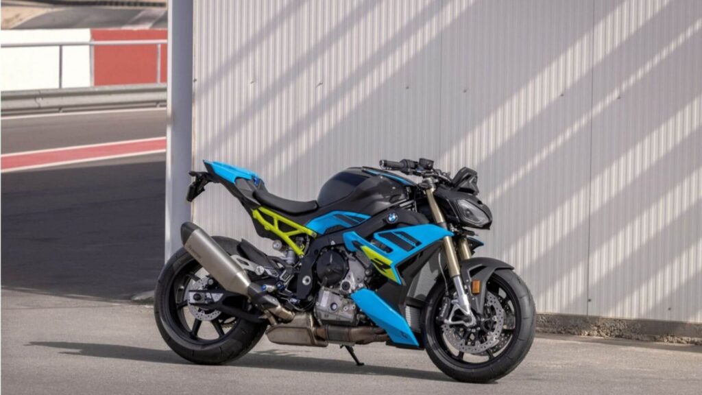 bmw s 1000 r azul com detalhes em amarelo e preto parada do lado de um galpao 