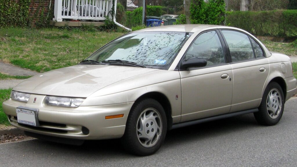 Chevrolet Saturn bege estacionado na beirada da calçada.