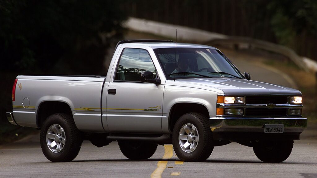 Chevrolet Silverado prata parada no meio da pista na diagonal.