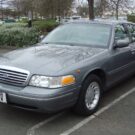 Ford Crown cinza escuro em uma vaga de estacionamento.