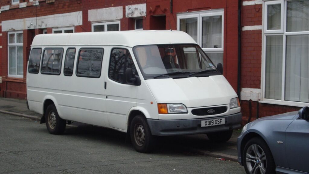 Ford Transit branca estacionada na beirada da calçada.