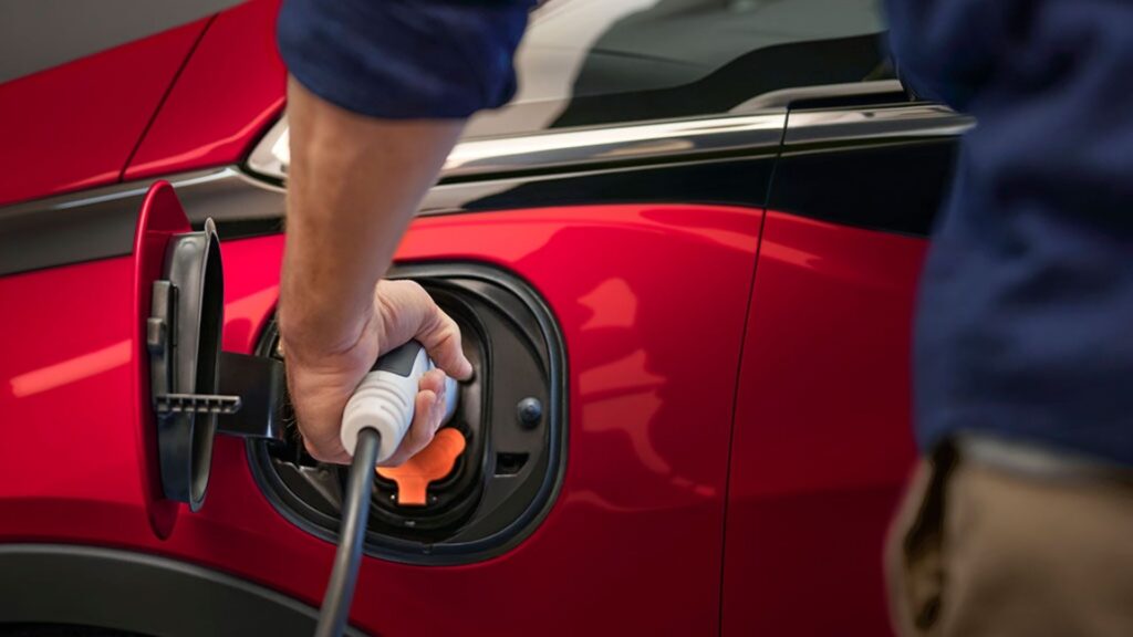 Pessoa carregando seu carro elétrico vermelho.