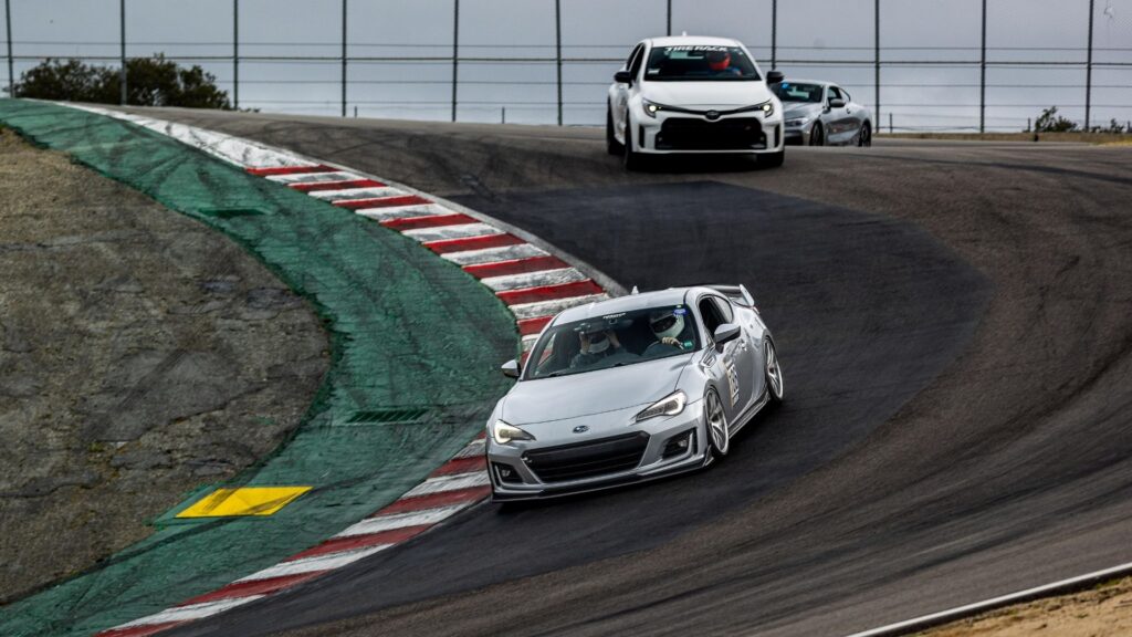 Carro cinza fazendo uma curva com um carro branco atras.