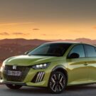 Peugeot e-208 verde na estrada com um por do sol no fundo.