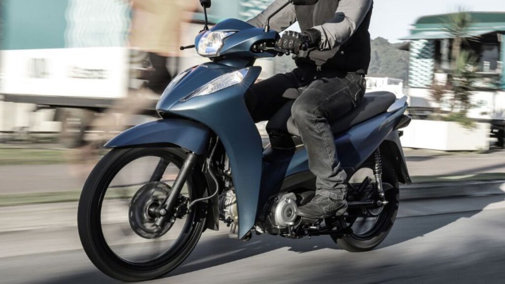Honda Biz 125 azul com um motociclista em cima.