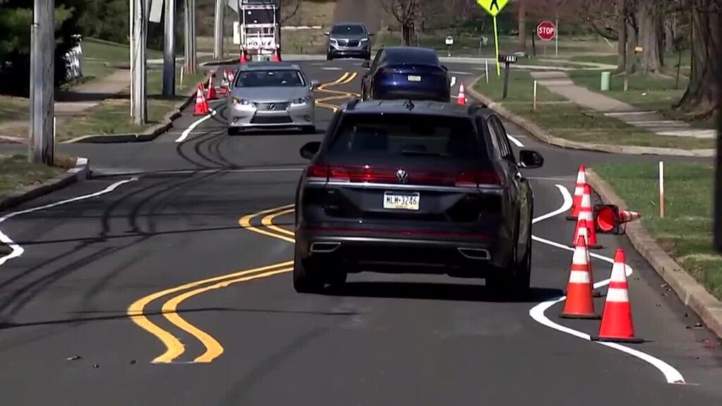 Carro preto passando na estrada com faixas tortas.
