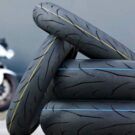 4 pneus novos com uma moto branca no fundo.