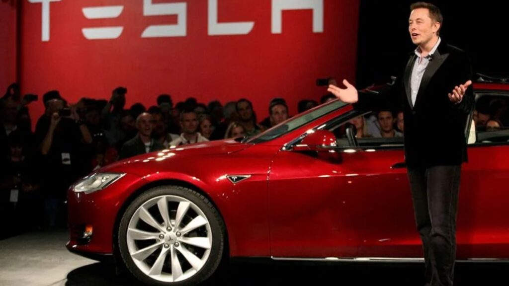 Carro vermelho da tesla parado do lado do Elon Musk.