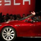 Carro vermelho da tesla parado do lado do Elon Musk.