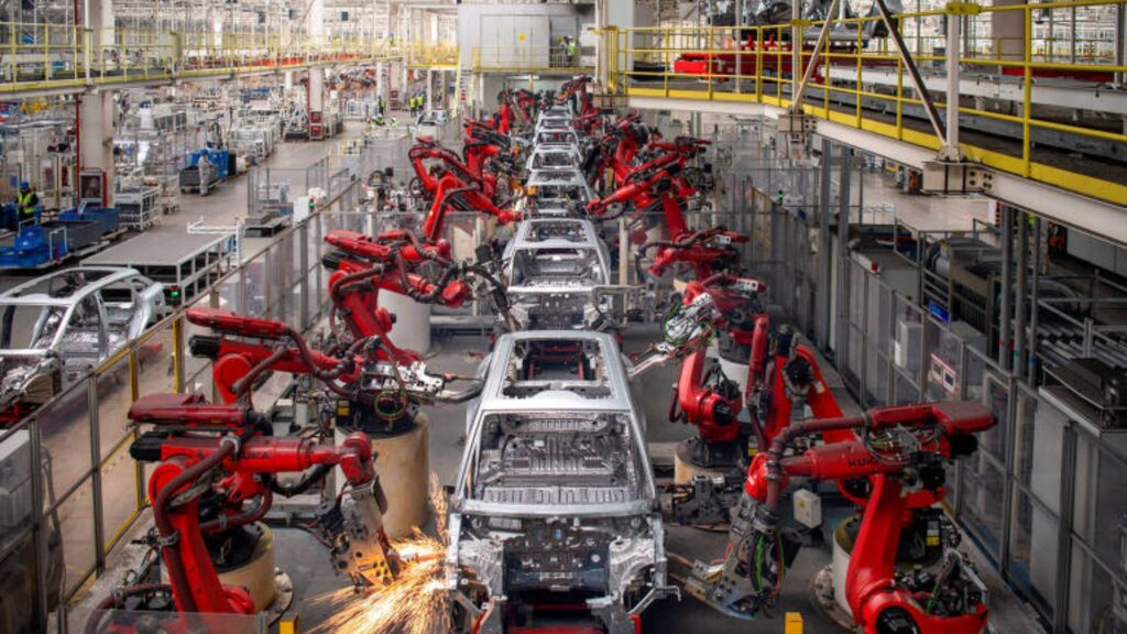 Robôs fabricando carros elétricos pratas.