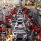 Robôs fabricando carros elétricos pratas.