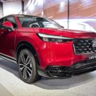 Honda HR-V 2026 vermelho na diagonal em uma exposição do lado de um telão.