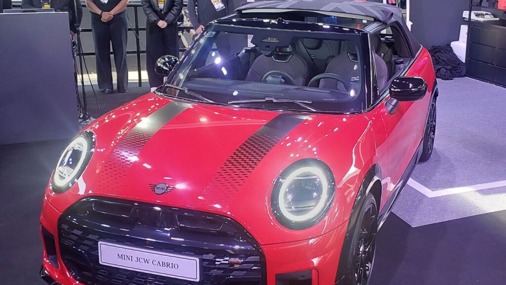 MINI JCW vermelho com listras pretas na diagonal com faróis acesos.