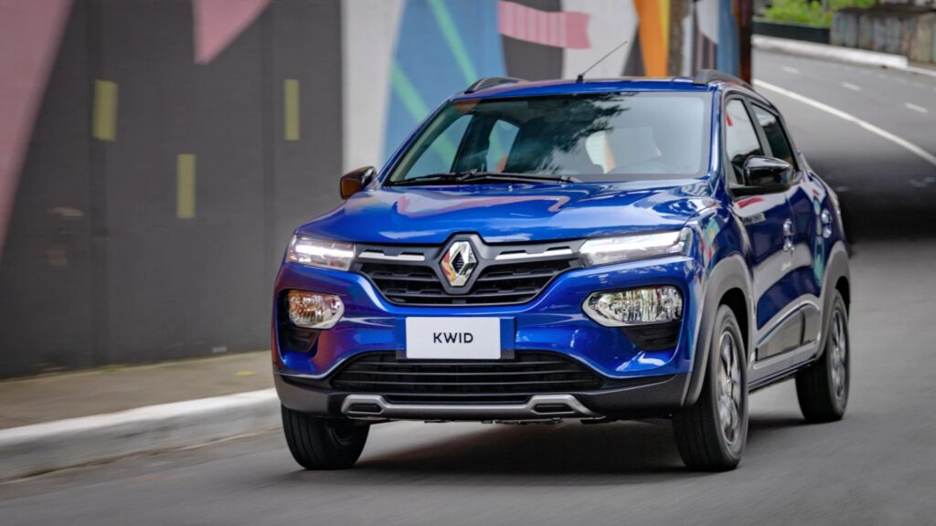 Renault Kwid 2026 azul na estrada com os faróis ligados.