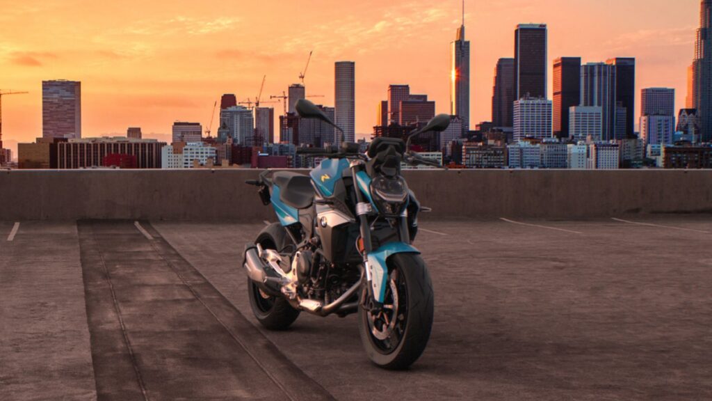 BMW F 900 R 2026 azul parada na diagonal em cima de um prédio com um por do sol no fundo.