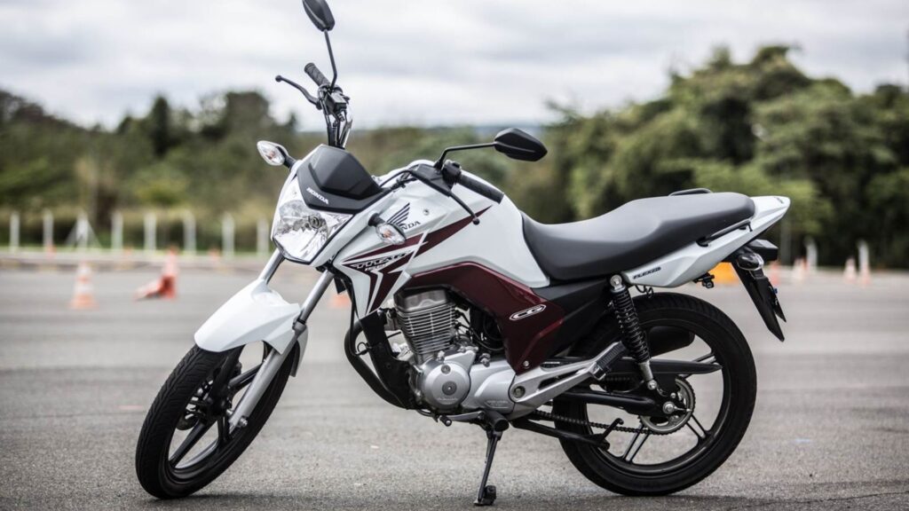 Honda CG 150 parada na diagonal branca.