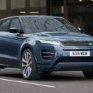 Range Rover Evoque 2026 azul em movimento na estrada com os faróis acesos.
