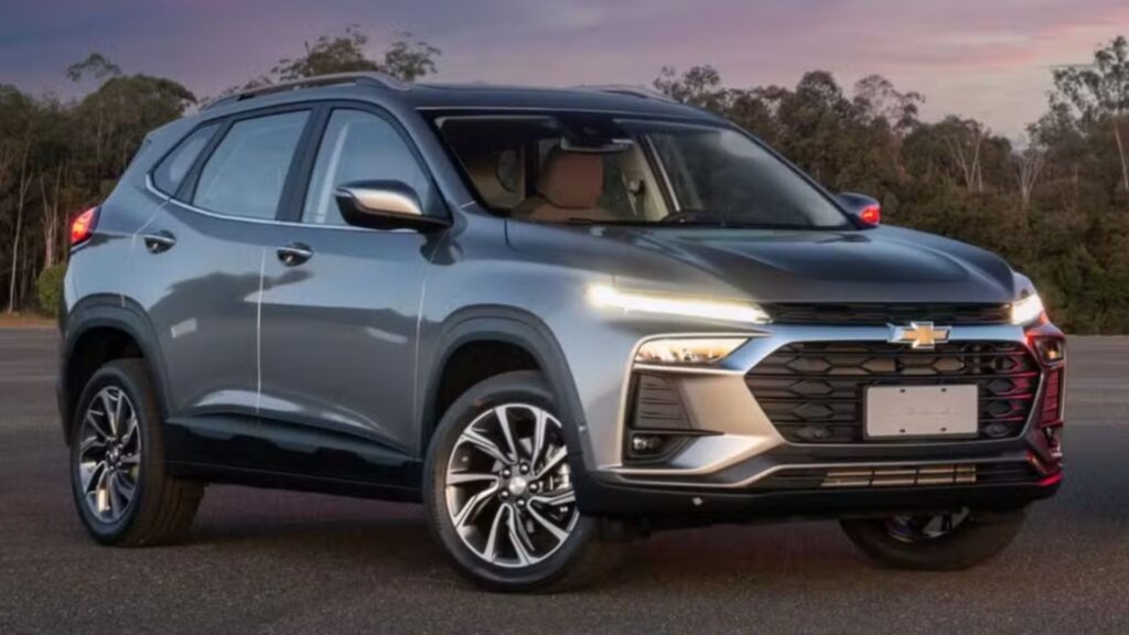 Chevrolet Tracker 2026 cinza parado na diagonal com os faróis acesos.
