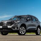 Haval H6 One 2026 cinza parado na diagonal com um céu azul no fundo.