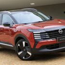 Nissan Kicks 2026 vermelho parado na diagonal em uma garagem.