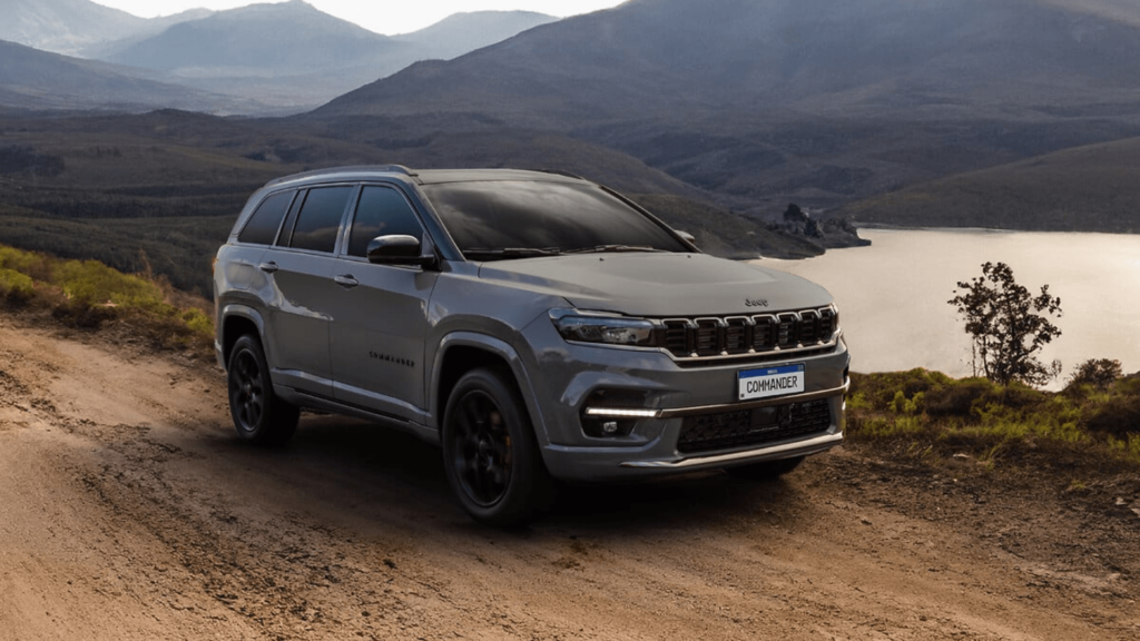 Jeep Compass cinza parado na beirada da estrada de terra com um lago e uma montanha no fundo.