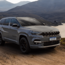 Jeep Compass cinza parado na beirada da estrada de terra com um lago e uma montanha no fundo.