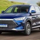 BYD Song Plus azul em movimento na estrada com um gramado verde no fundo.