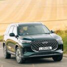 Chery Tiggo 8 2026 verde fazendo uma curva com uma plantação de trigo no fundo.