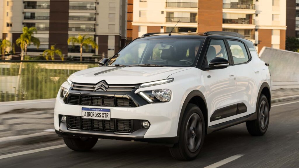 Citroën Aircross 2026 branco em movimento na estrada com os faróis acesos e com uns prédios no fundo.