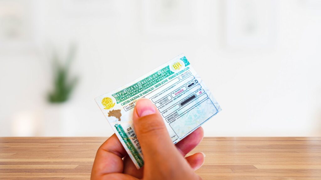 Pessoa segurando um documento verde chamado CNH com uma mesa na frente.