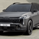 Kia Sportage 2026 cinza parado na diagonal com os faróis ligados.