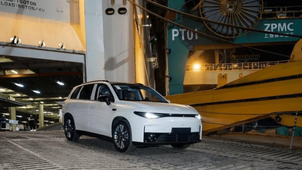 Leapmotor C10 branco saindo de um navio no porto de noite com os faróis ligados.