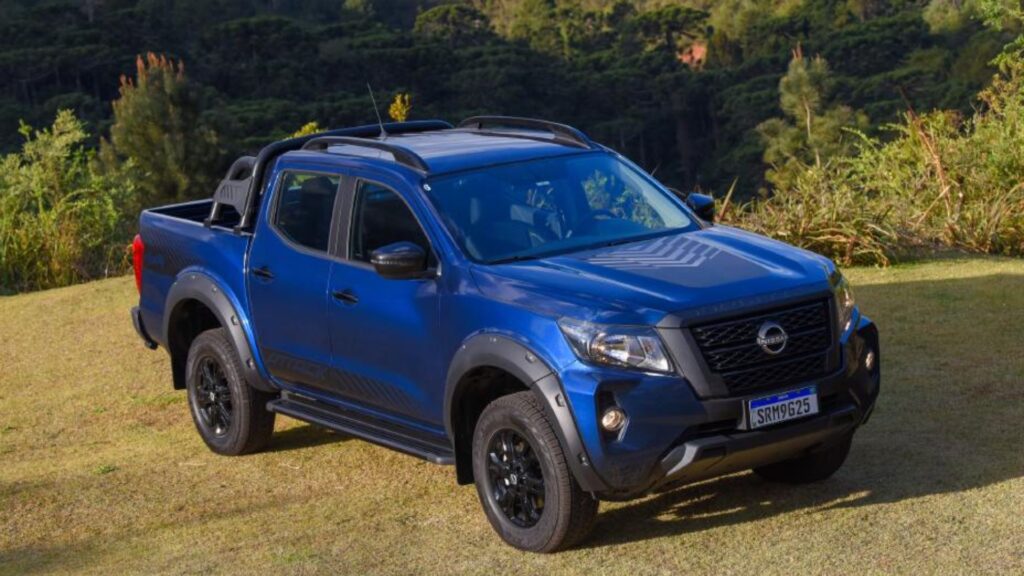 Nissan Frontier azul parado na diagonal em cima de um gramado verde.