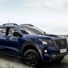 Nissan Frontier azul parado na diagonal em um campo verde.