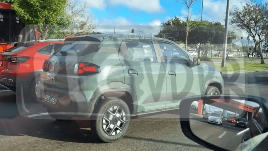 Novo Kwid E-Tech verde parado na estrada esperando a sinaleira abrir.