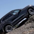 Lateral do Porsche Cayenne elétrico preto que esta escalando uma pedra.