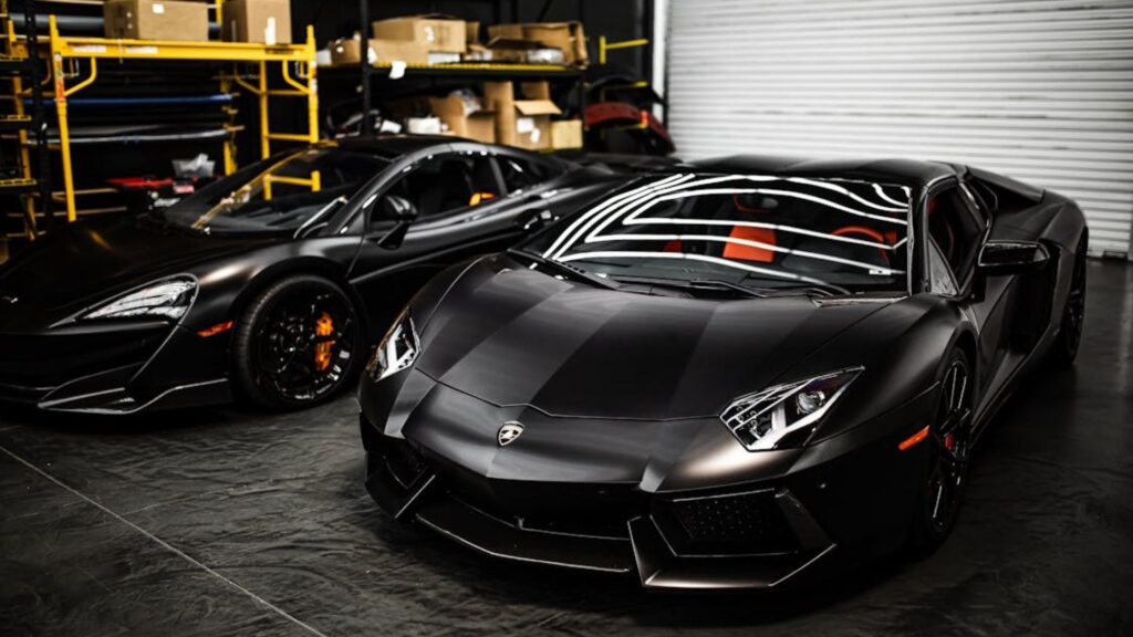 Dois carros de luxos pretos parados dentro de uma garagem.