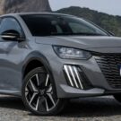 Peugeot 208 2026 Hybrid na diagonal em cima de um asfalto com uma montanha no fundo.