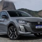 Peugeot 208 2026 híbrido cinza parado na diagonal com o Pão de açúcar no fundo.
