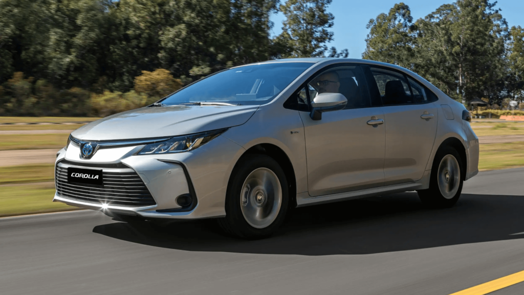 Toyota Corolla 2026 prata em movimento na estrada com uma vegetação no fundo.