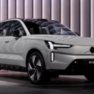 Volvo EX90 2026 cinza parado na diagonal com os faróis ligados.